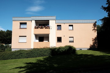 Modernes Mehrfamilienhaus mit Flachdach und Balkons in Beige und Naturfarben vor blauem Himmel im...