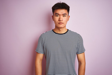 Obraz premium Young asian chinese man wearing striped t-shirt standing over isolated pink background with serious expression on face. Simple and natural looking at the camera.