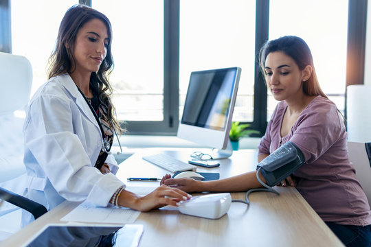 Pretty young woman gynecologist checking the blood pressure of her pregnant patient in the clinic.