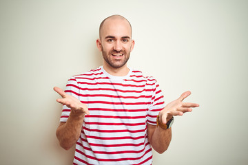 Young bald man with beard wearing casual striped red t-shirt over white isolated background smiling cheerful offering hands giving assistance and acceptance.