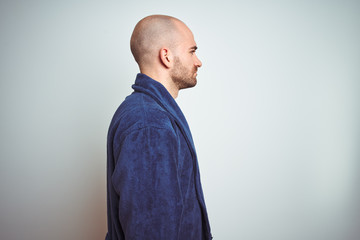Young man wearing blue bathrobe, relaxed lifestyle over isolated background looking to side, relax...