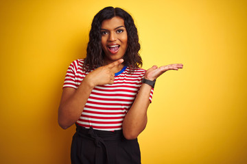 Transsexual transgender woman wearing stiped t-shirt over isolated yellow background amazed and smiling to the camera while presenting with hand and pointing with finger.