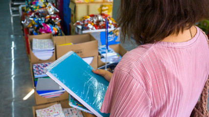 Student girl comparing school products in stationery shop. Back to school concept photo in a hypermarket. Beginning of the new training / education season. Blurred background.