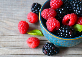 Fresh ripe organic blackberries and raspberries in a blue bowl on rustic wooden table.Summer berries.Healthy eating,vegan food or diet concept. Selective focus.