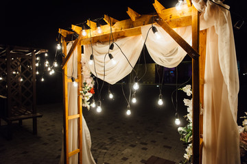 night wedding ceremony. A garland of light bulbs. candles in glass flasks in the evening.
