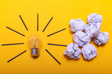 Inspiration concept crumpled paper and light bulb metaphor for good idea. White crumpled paper and light bulb on yellow background, flat lay.
