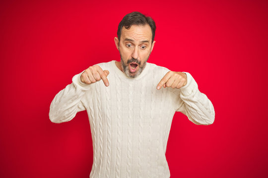 Handsome middle age senior man with grey hair over isolated red background Pointing down with fingers showing advertisement, surprised face and open mouth