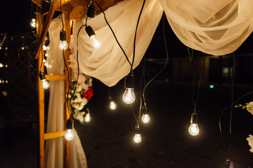 night wedding ceremony. A garland of light bulbs. candles in glass flasks in the evening.