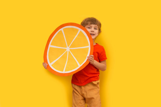 Funny Kid With Orange Segment From A Cardboard On A Yellow Background. Healthy Food. Concept Summer Lifestyle.