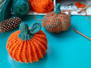 Knitted orange pumpkin, yarn balls and crochet hook on wooden turquoise table