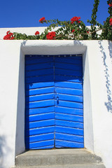 Architektura Santorini - niebieskie drzwi otoczone kwiatami na tle białej ściany