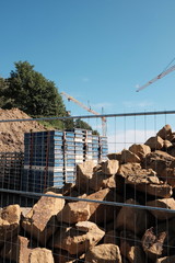 Baustelle mit Drahtzaun, Naturstein und Baumaterial auf Paletten vor blauem Himmel im Sonnenschein in Oerlinghausen bei Bielefeld am Hermannsweg im Teutoburger Wald in Ostwestfalen-Lippe