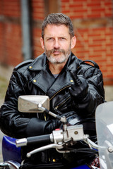 handsome man in black leather sitting on his motorbike and showing the middle finger