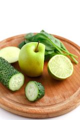 Sliced green apple, cucumber and lime on a wooden cutting board.