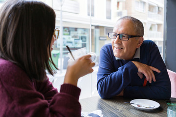 Senior man having a conversation with woman drinking coffee and relaxing, chatting at restaurant