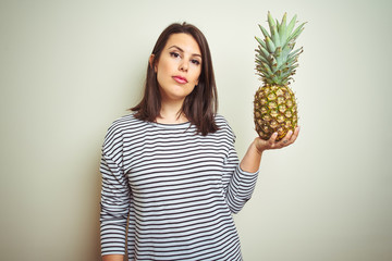Young beautiful woman holding tropical fruit pineapple over isolated background with a confident...