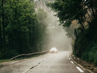 Chorance, France - Aug 11, 2017: White Citroen car silhouette driving fast on mountain road in the Vercors Massif on a misty day with fog and tall mountain in background