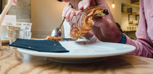 Side view of man and woman eating delicious pain au chocolat early in the morning in French cafe