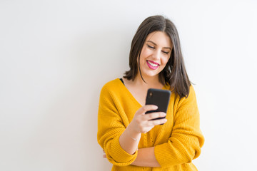 Fototapeta premium Beautiful brunette young woman smiling confident using smartphone over isolated white background wearing casual yellow sweater
