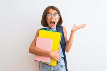 Beautiful student child girl wearing backpack glasses books over isolated white background very happy and excited, winner expression celebrating victory screaming with big smile and raised hands
