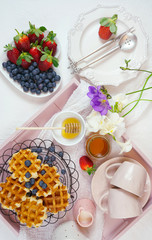 Obraz na płótnie Canvas Modern blush pink breakfast tray with waffles, honey and fruit.