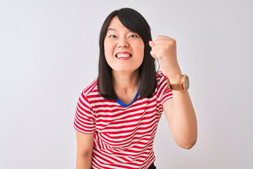 Young beautiful chinese woman wearing red striped t-shirt over isolated white background angry and mad raising fist frustrated and furious while shouting with anger. Rage and aggressive concept.