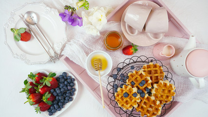 Modern blush pink breakfast tray with waffles, honey and fruit.