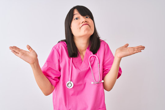 Young beautiful Chinese nurse woman wearing stethoscope over isolated white background clueless and confused expression with arms and hands raised. Doubt concept.