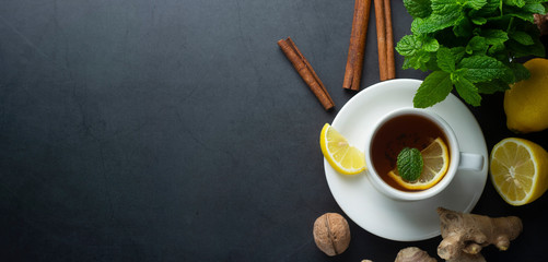 Cup of ginger tea with lemons and mint leaves on dark background. Banner, cold and autumn time.