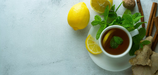 Glass cup of ginger tea with lemons and mint leaves on light background. Ginger tea, drink, cold and autumn time. Banner.