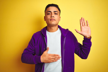 Young brazilian man wearing purple sweatshirt standing over isolated yellow background Swearing...