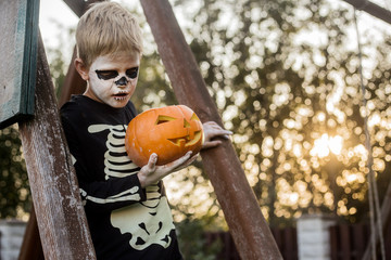 Happy young blond hair boy with skeleton costume holding jack o lantern. Halloween. Trick or treat. Outdoors portrait