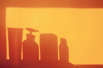 Shadows from tubes with balm and shampoo on orange background. Cosmetic beauty mockup. Bathroom hygiene.