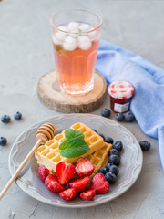 Plate of waffles decorated with honey and fresh berries and Glass of fresh red fruit juice on gray stone background. Food concept. Top view.