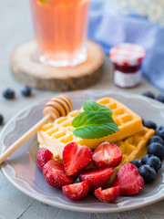 Plate of waffles decorated with honey and fresh berries on gray stone background. Food concept. Photo with selective focus