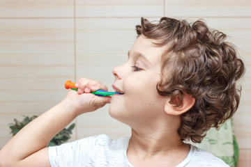 Happy little boy brushing his teeth in bathroom in front of mirror, oral hygiene