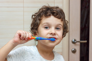 Happy little boy brushing his teeth in bathroom in front of mirror, oral hygiene