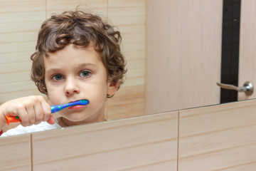 Little boy brushing his teeth in bathroom in front of mirror, oral hygiene