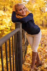 In the autumn, yellow leaves circle the bridge. A girl is standing and looking around in white jeans