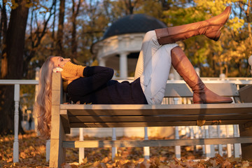 Autumn girl talking on the phone while lying on a bench in a park, after a walk