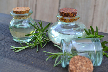 Rosemary essential oil in glass bottles with cork stoppers and fresh rosemary herb on wooden rustic background