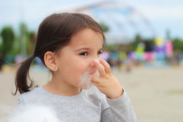 Little funny white girl with tails with narrow eyes holds cotton candy with his lips while walking...