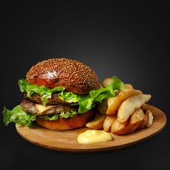 Appetizing burger with sauce and side dish on a wooden board.