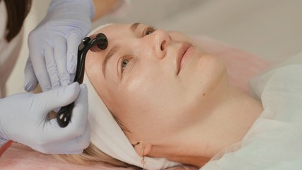 Close-up portrait of woman having beauty skin treatment. Therapist preparing skin with derma roller.