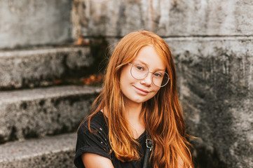 Outdoor portrait of sweet little girl with red hair, wearing eyeglasses