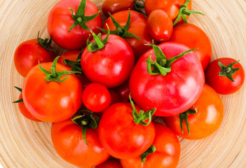 Wooden dish with different ripe tomatoes on white background.