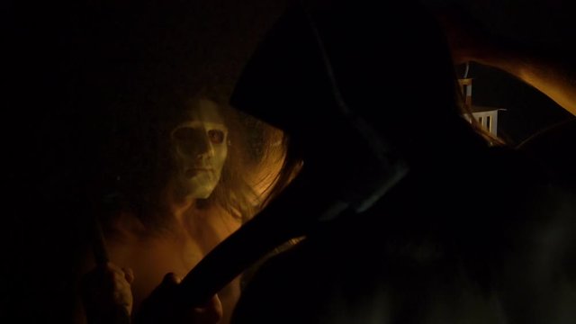 halloween, a masked maniac, looking at himself in a mirror, holding a lamp with candles in his hands