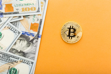 Golden Bitcoin coin on a us dollars close up on the orange background with copy space.