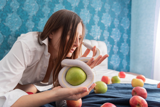 beauty young woman with white american queen snake and green apple lying on the bed. Around scattered apples. The image of biblical eve in the modern world