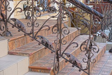 Staircase with  concrete steps and iron brown handrails with a forged pattern near the wall 